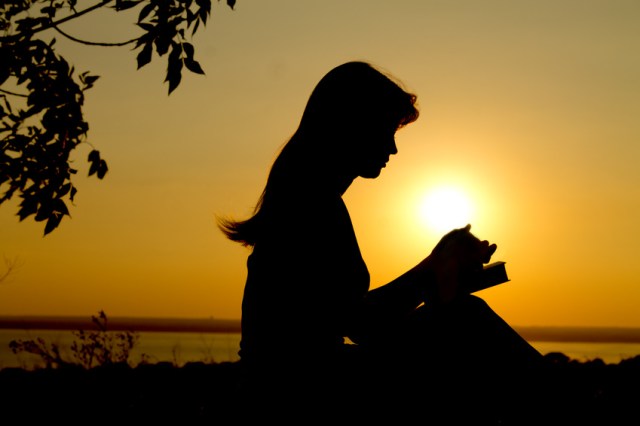silhouette of a girl praying with the Bible